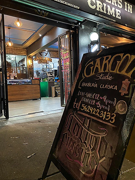 Pizarrón en la entrada con letra dorada: Gárgola Studio, barbería clásica, y el teléfono para citas
