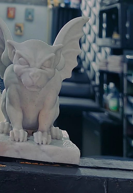 Estatuilla blanca de una gárgola con alas sobre el mostrador de la barbería