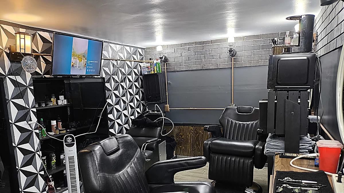 El salón de Gárgola Studio: dos sillones de barbero negros, el muro de mosaico blanco y negro y la pared de ladrillo gris con un tubo de latón
